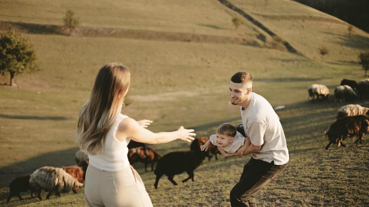 A joyful family with a child in a pastoral setting, embracing countryside life with grazing sheep.